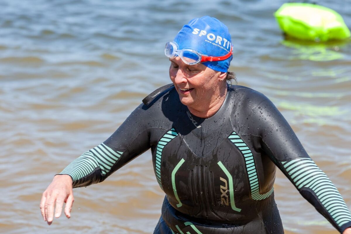 Swimmer in a wetsuit and Sportiva swim cap wading out of the lake after an open-water swim